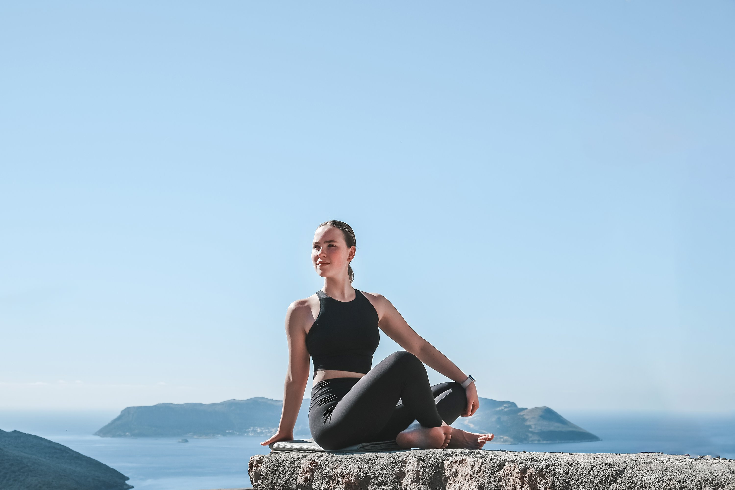 Person in athletic wear sitting calmly on a ledge overlooking the sea